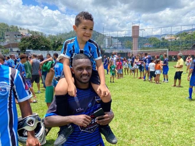 Pelé carregando o filho Luiz Fernando, no dia da consagração de quem persistiu e buscou o sucesso com a camisa do bairro em que reside