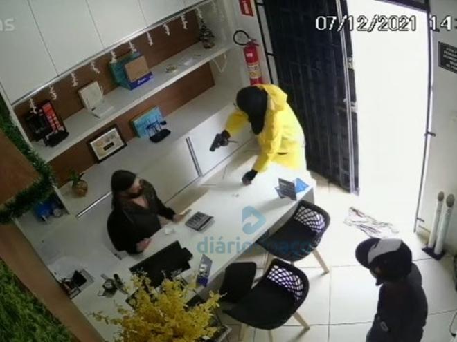 O momento que o assaltante exige os pertences da funcionária que atendia um cliente no escritório